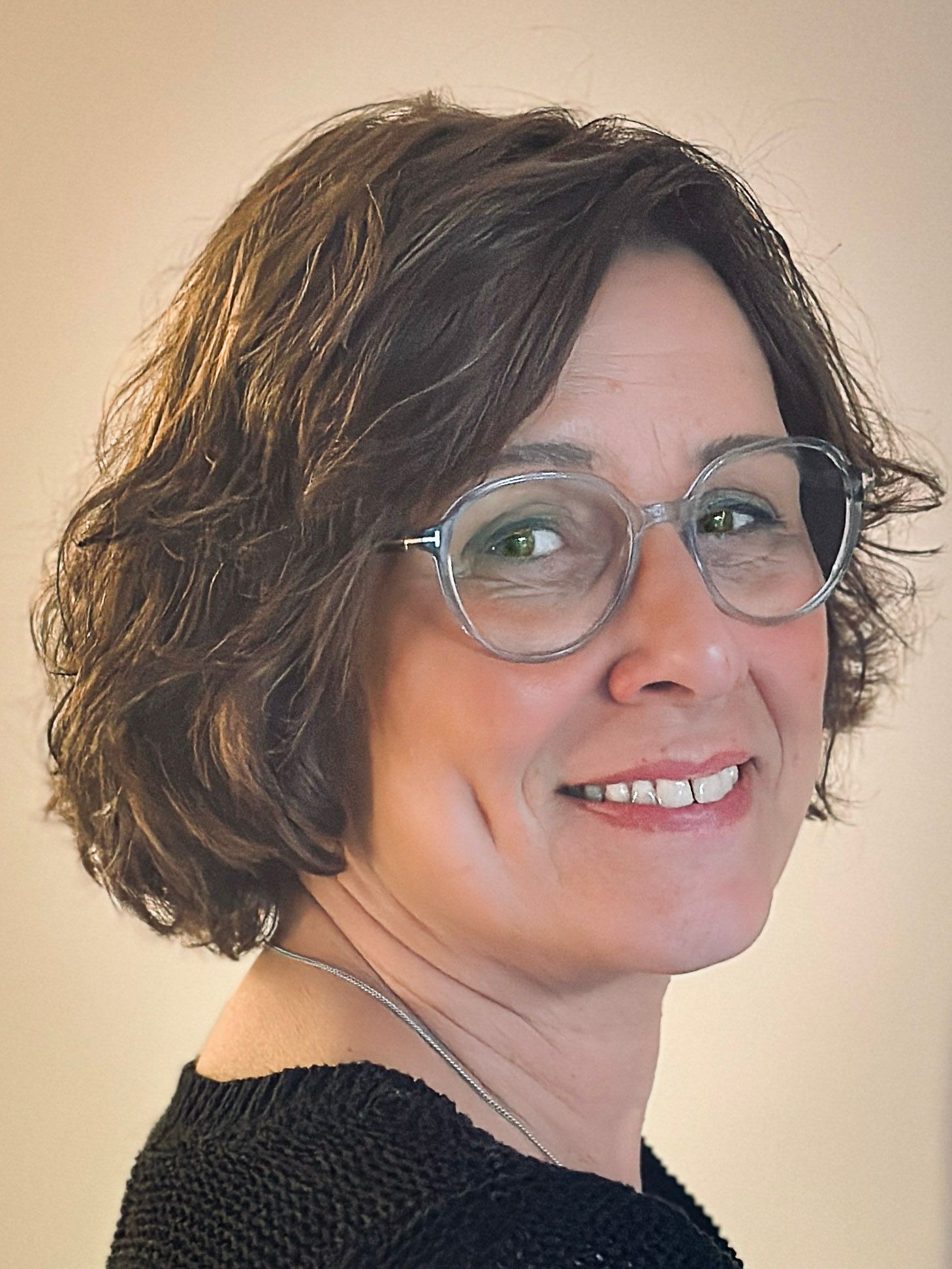 Frau mit kurzen braunen Haaren, die eine Brille trägt, lächelt und in die Kamera schaut.