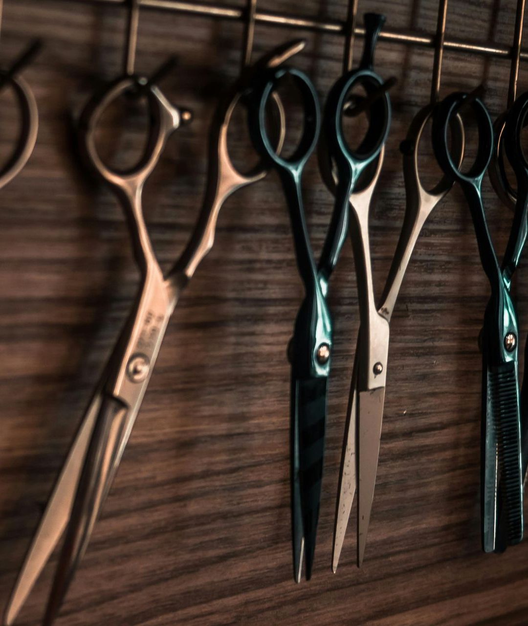 An einer Holzwand hängen Haarschneidescheren, einige offen, einige geschlossen, mit Metallhalterungen.