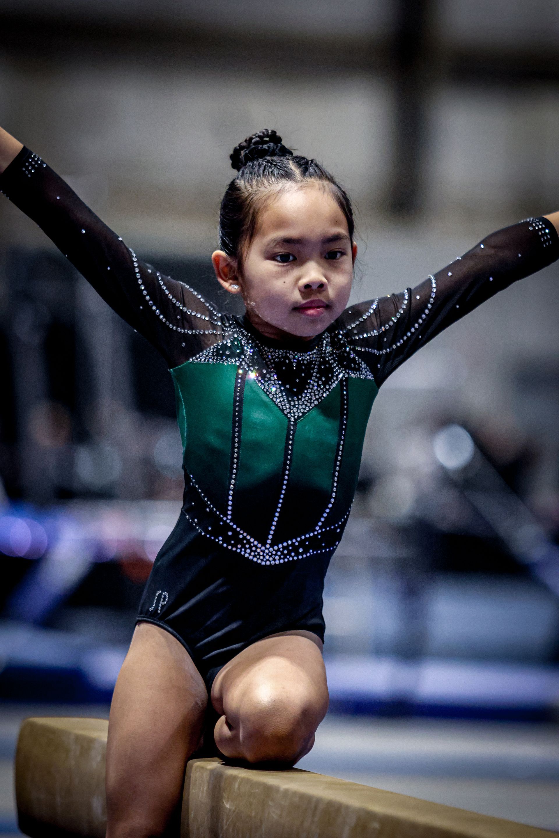 A young girl is sitting on a balance beam with her arms outstretched.