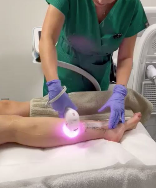 Una donna vestita di verde usa una macchina sulla gamba di un paziente.