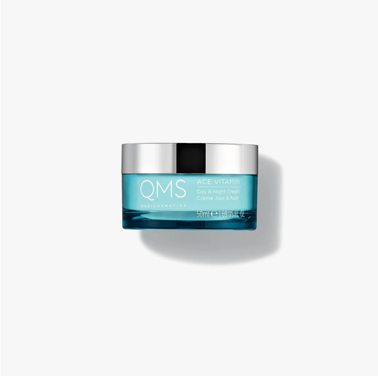 Un piccolo vasetto blu di crema per il viso qms è appoggiato su una superficie bianca.