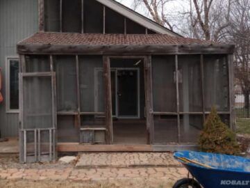 Dilapidated screened porch with a blue wheelbarrow in the foreground