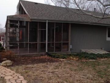 Weathered gray house with screened porch and stone walkway in a yard with bare trees