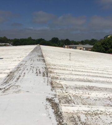 White corrugated rooftop under a cloudy blue sky, with trees and buildings in the distance.