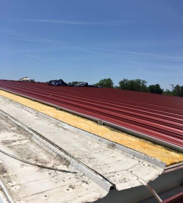 Red metal roof under a blue sky with white roofing in the foreground