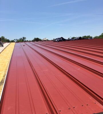 Red metal roof under a clear blue sky, with rooftop workers in the distance