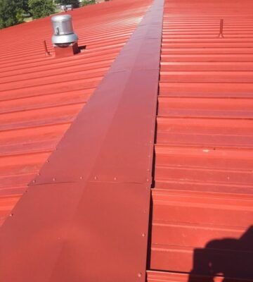 Red metal roof with a raised seam and a vent pipe on the left.