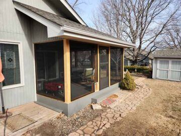 Screened patio attached to a gray house, with stone path and leafless trees in a yard