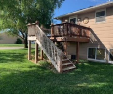 Wooden deck and stairs attached to a beige house in a grassy yard.