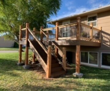 Wooden deck and staircase attached to a tan house in a grassy backyard.