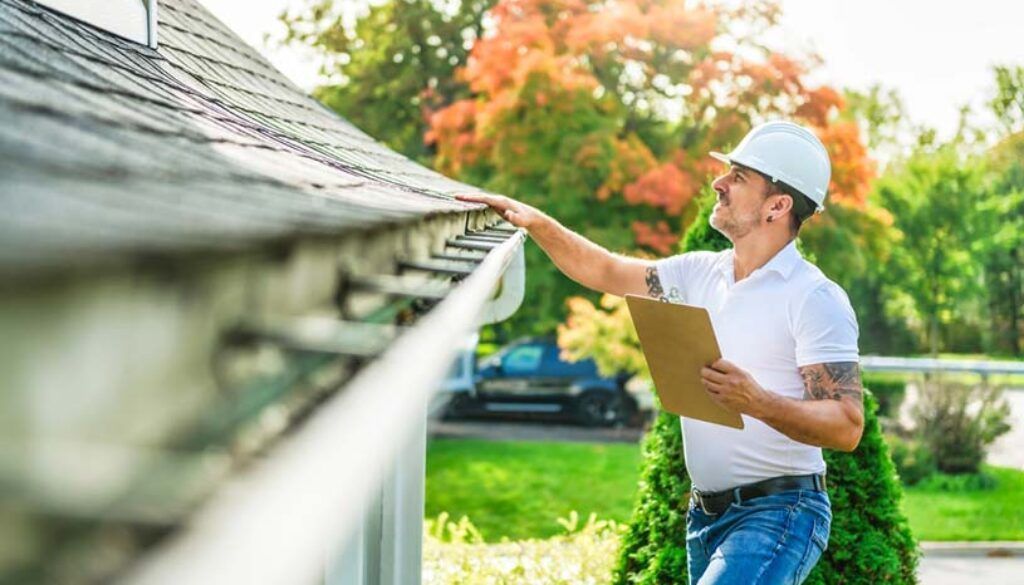 Worker inspecting a house gutter with a clipboard outdoors on a sunny day