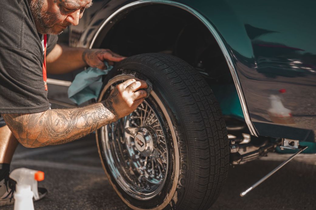 Person cleaning and polishing a car wheel and tire with a cloth outdoors
