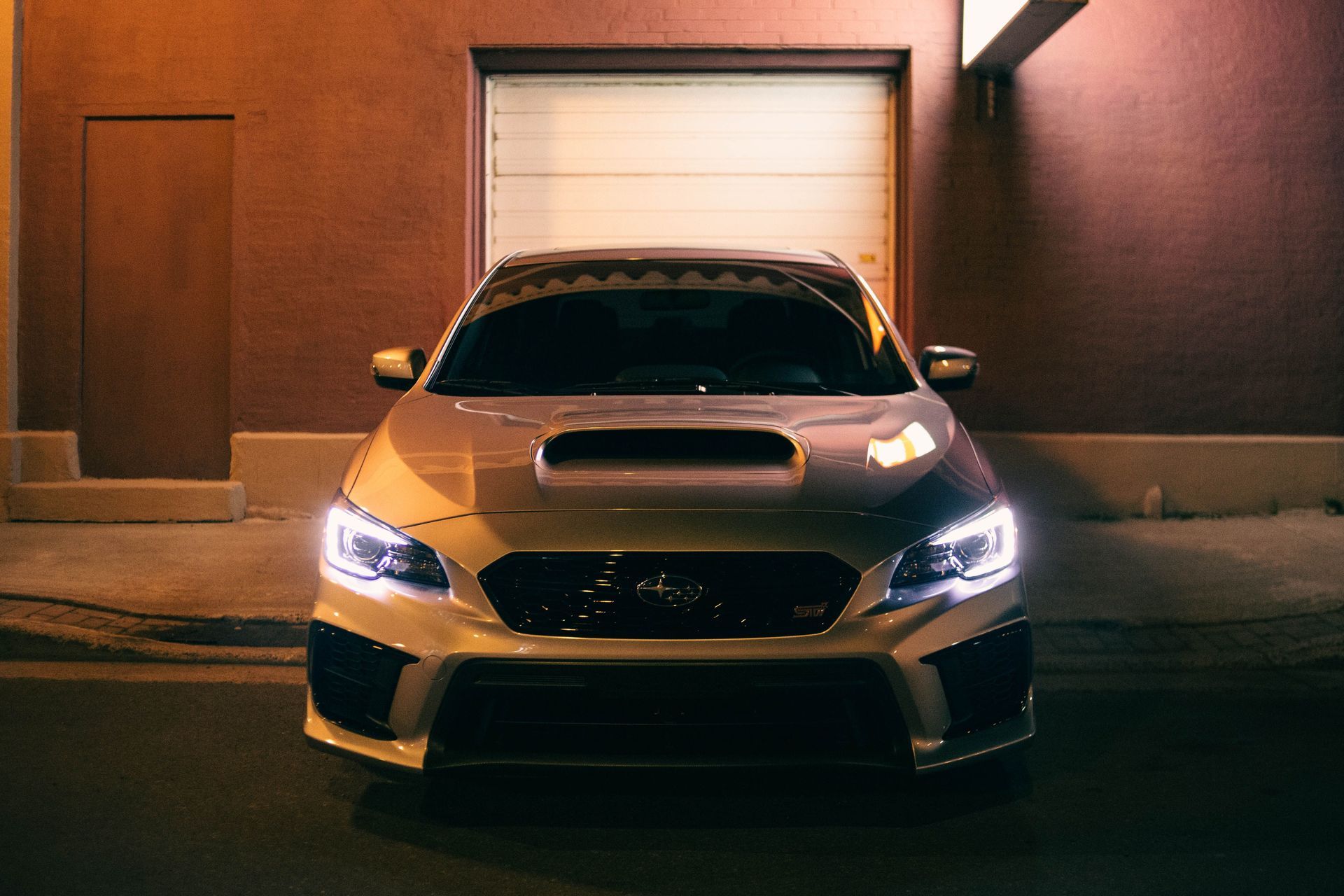 Silver sports car parked at night in front of a lit garage door