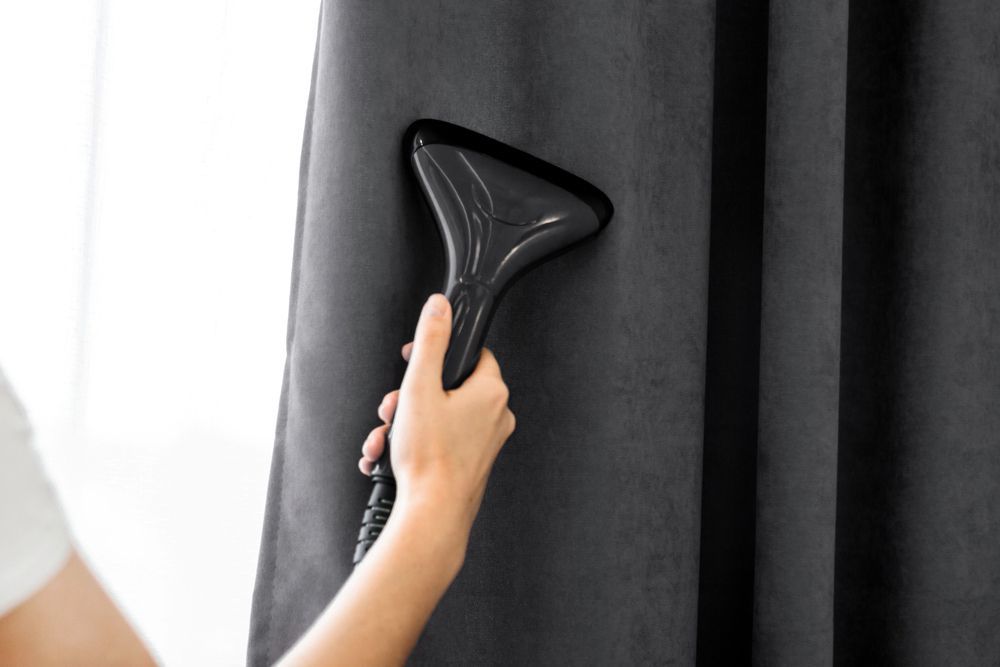 Vaporizador de ropa portátil utilizado sobre una cortina gris oscuro.