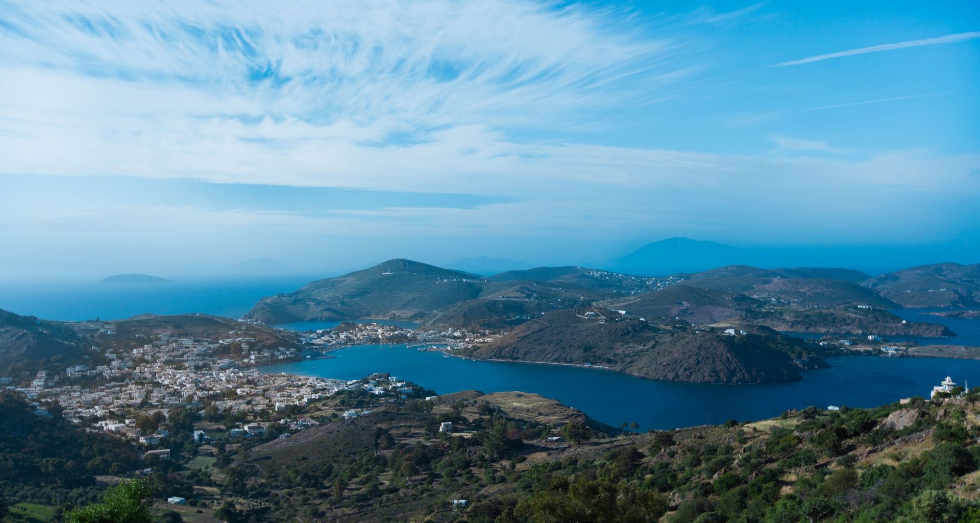 Coastal town nestled beside a blue lagoon and mountains under a bright sky.