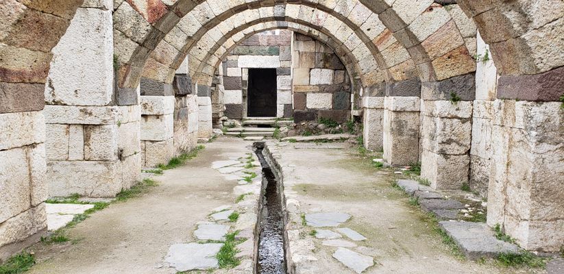 Stone arches over a long corridor with a water channel. The architecture appears old, in an outdoor setting.