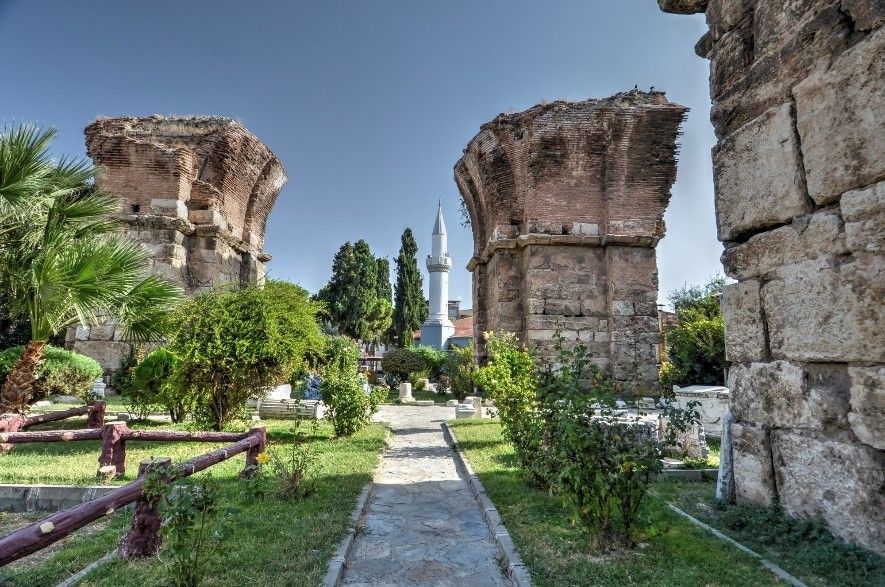 Ruins of an ancient structure with arched brickwork, grassy path, minaret in background.