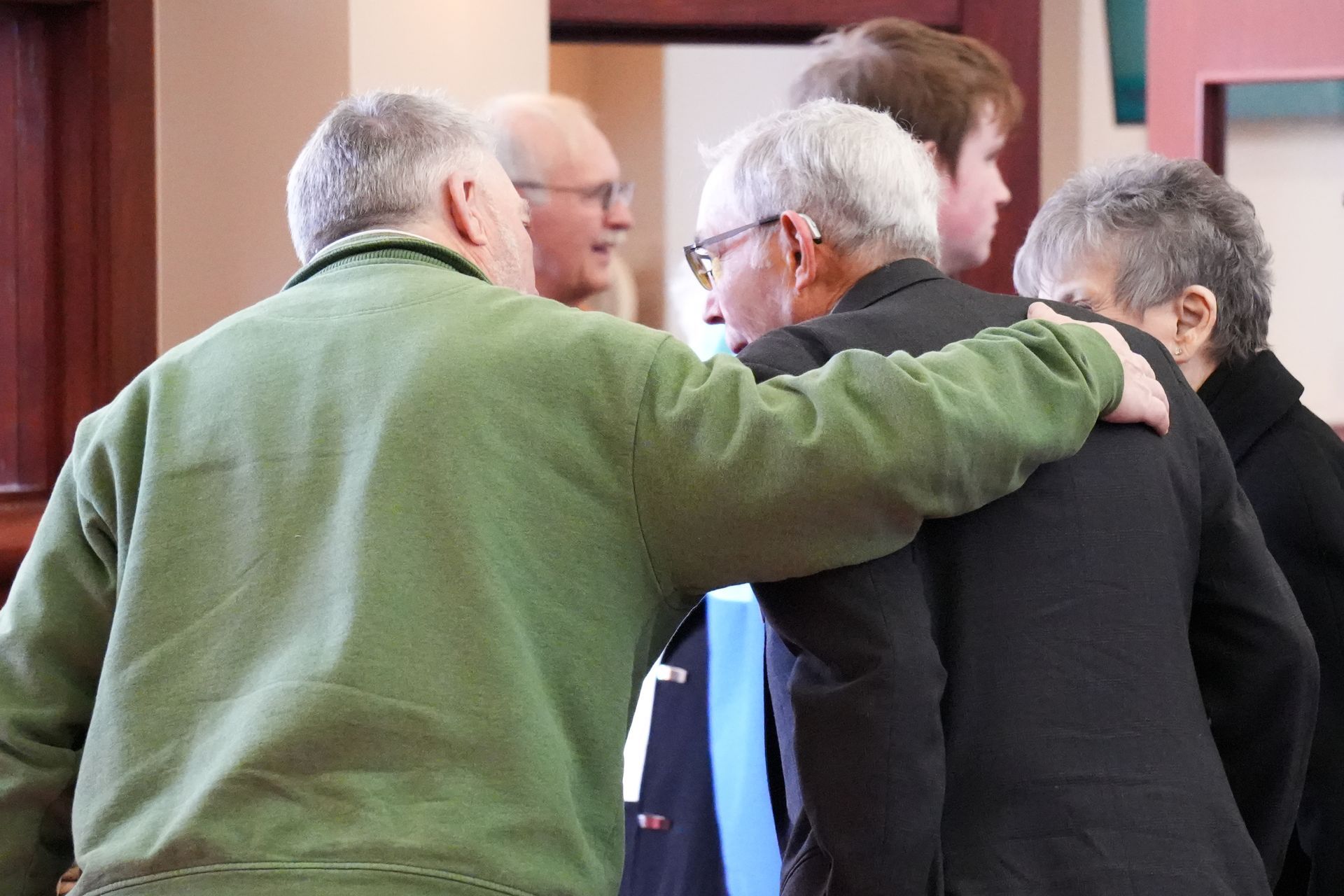 A group of people are standing in a room with their arms around each other.