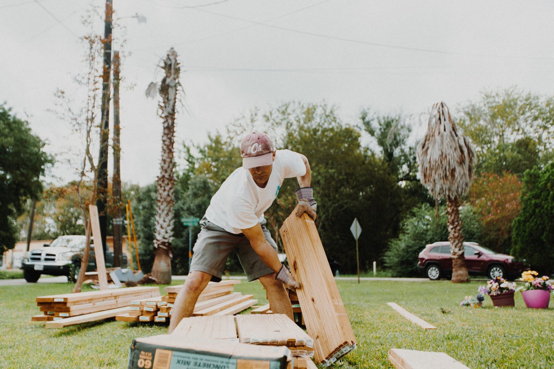 A man is lifting a piece of wood in a yard.