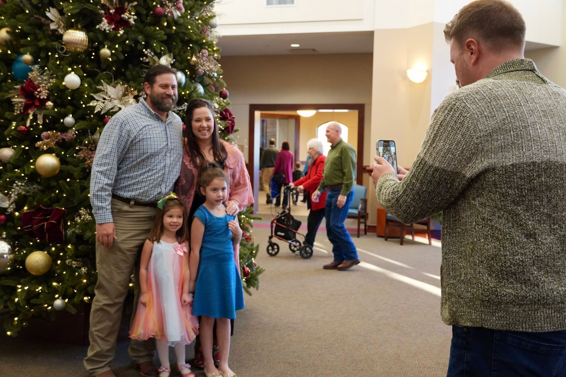 Family posing by decorated Christmas tree; another man taking their photo.