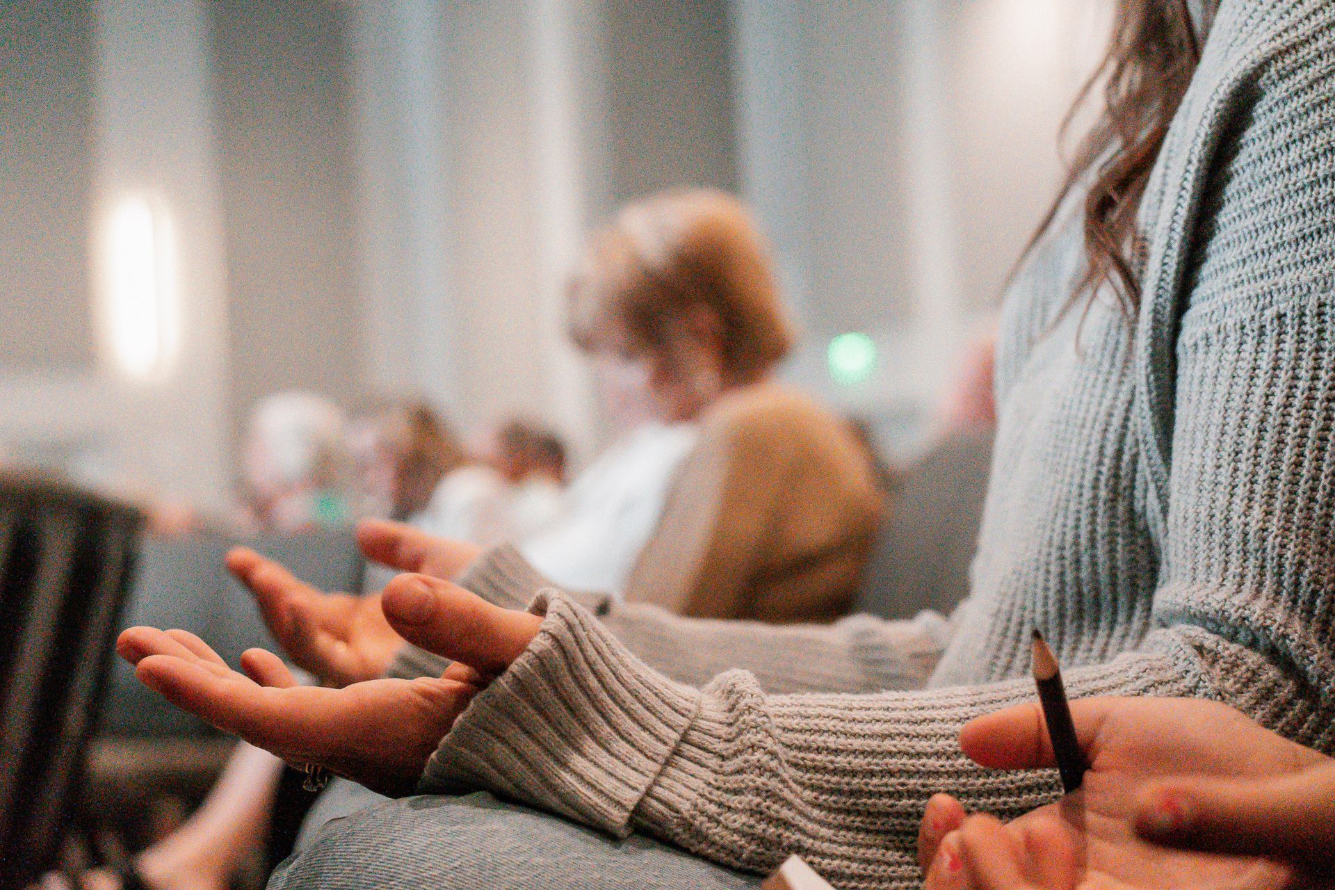 A group of people are sitting in a church with their hands open in prayer.