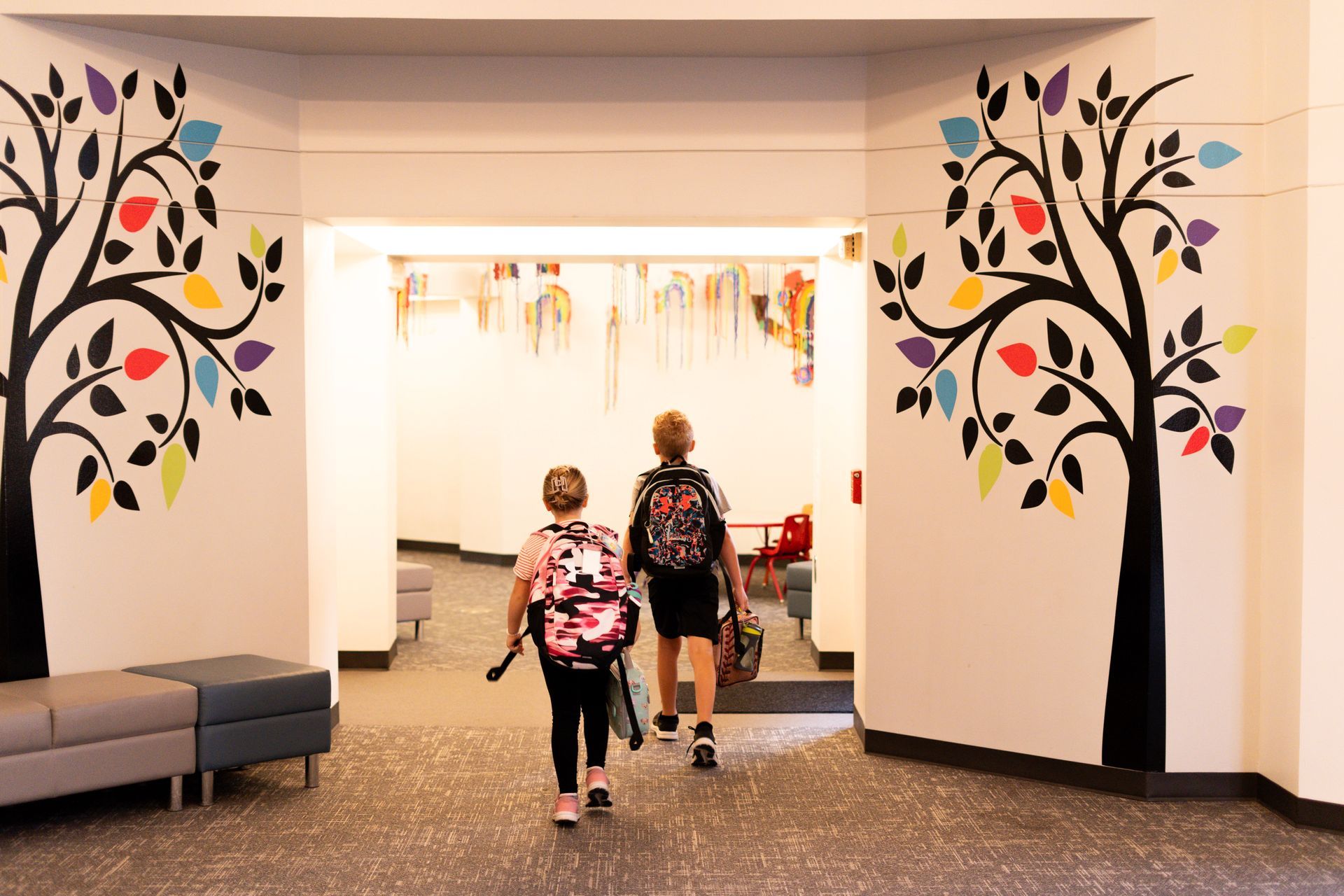 Two children are walking through a hallway with trees painted on the walls.