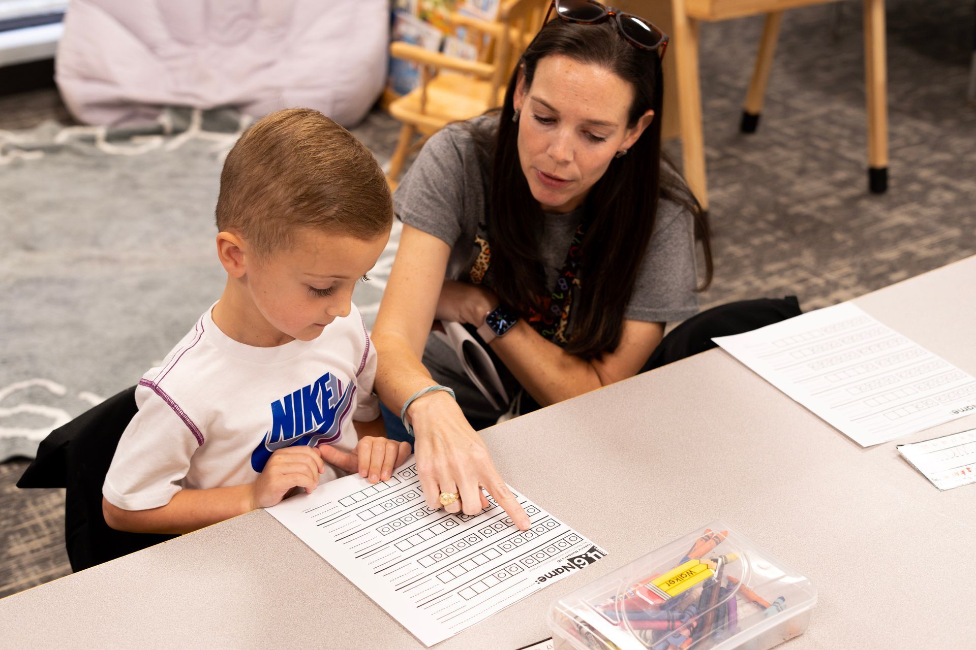 A woman is helping a young boy with his homework at a table.