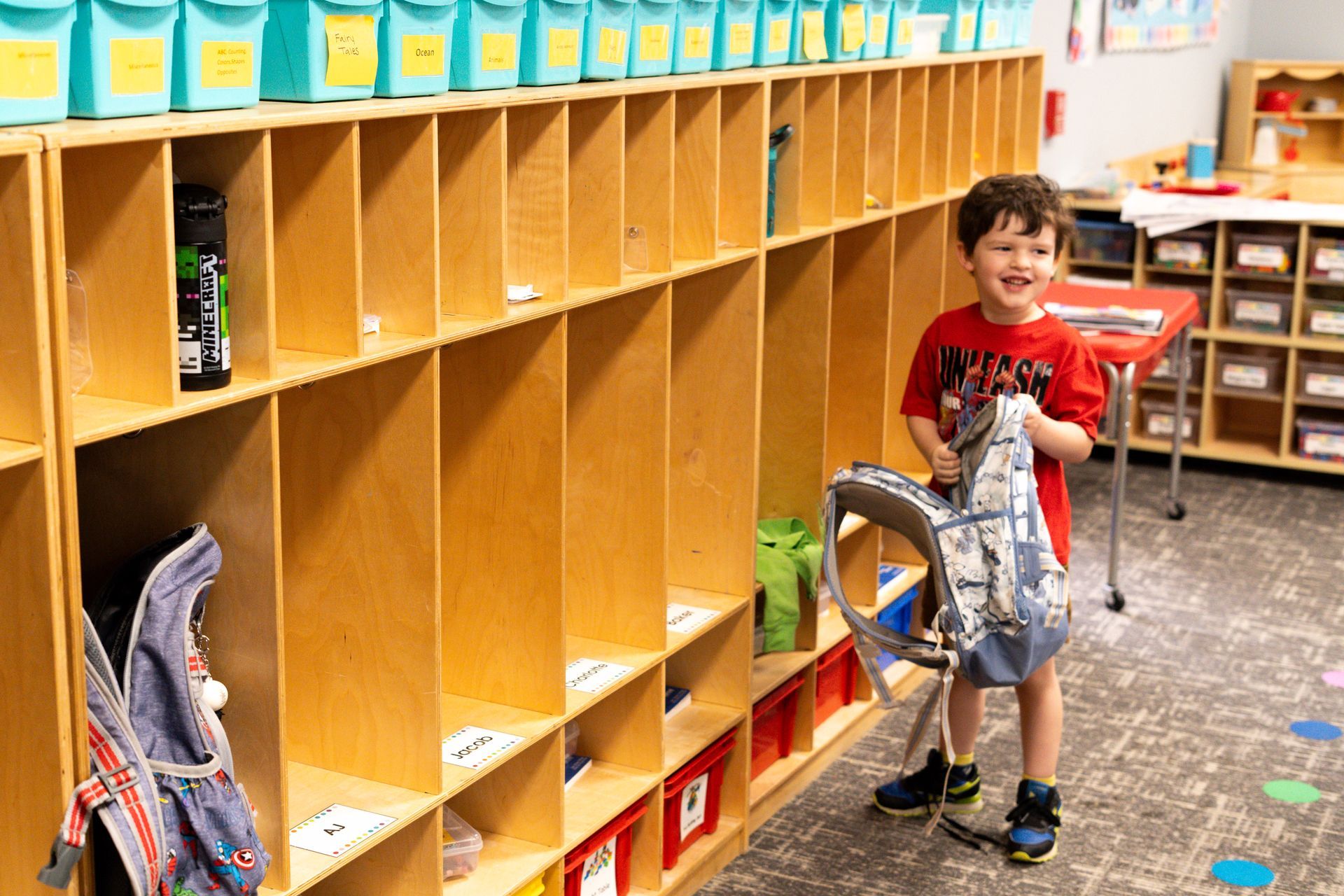 A young boy is standing in a locker room holding a backpack.