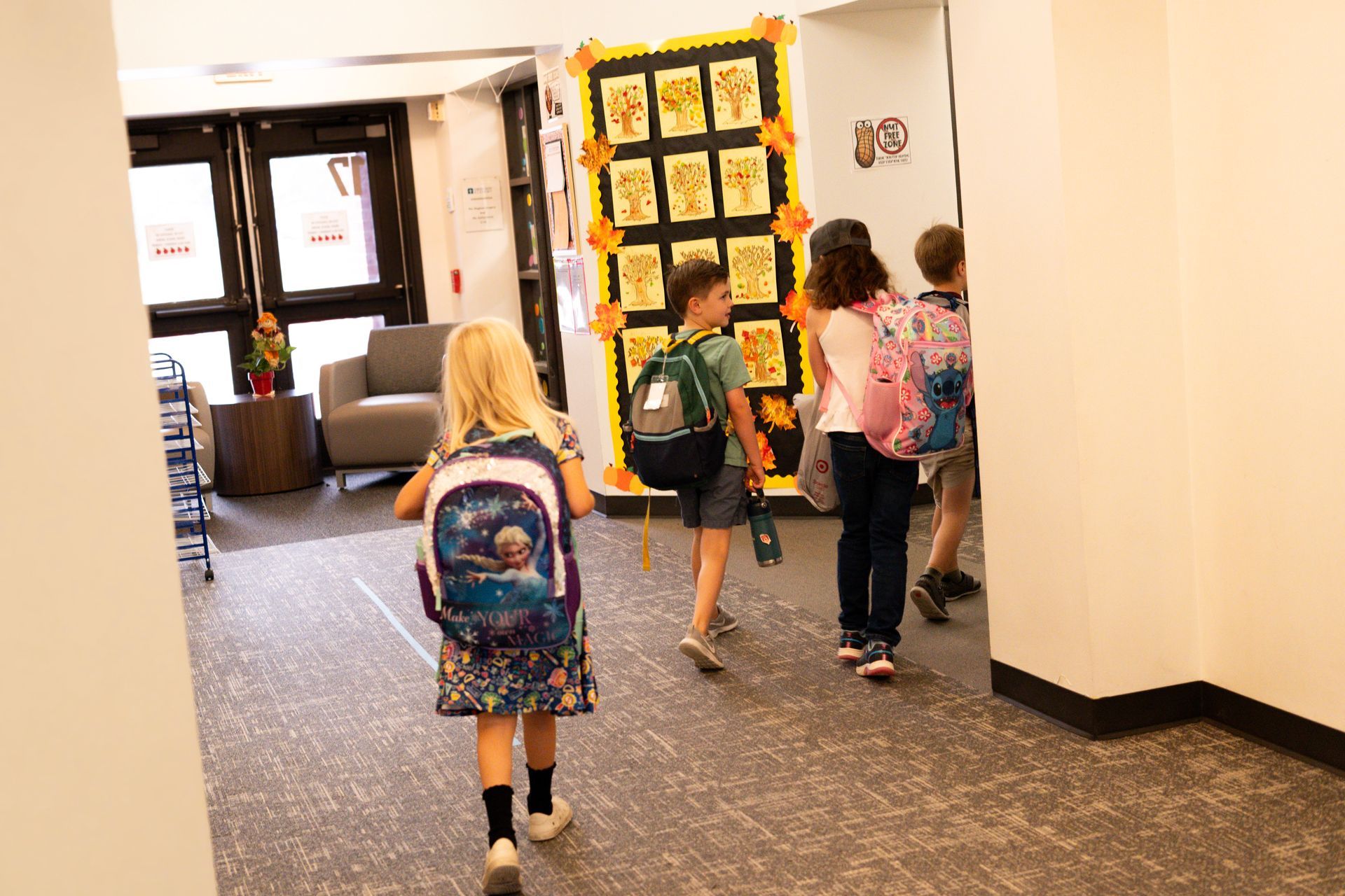 A group of children with backpacks are walking down a hallway.