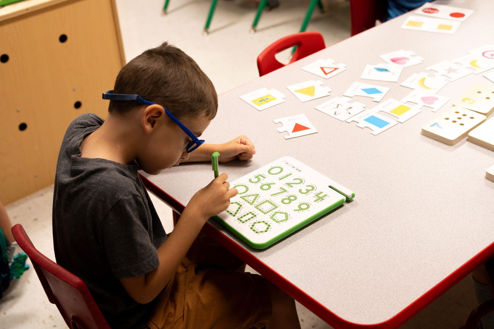 A young boy is sitting at a table writing on a piece of paper.