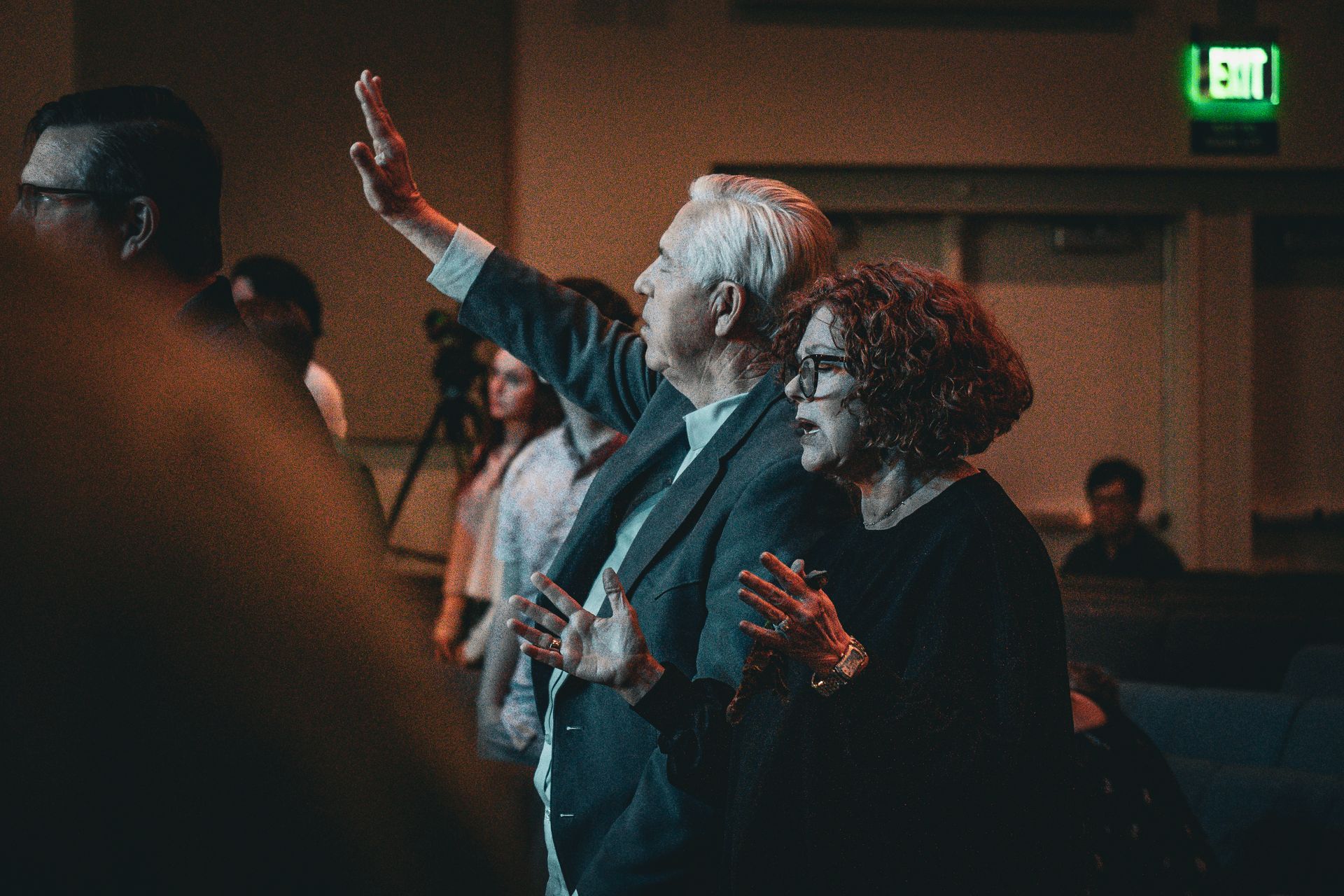 A man and a woman are worshiping with raised hands.