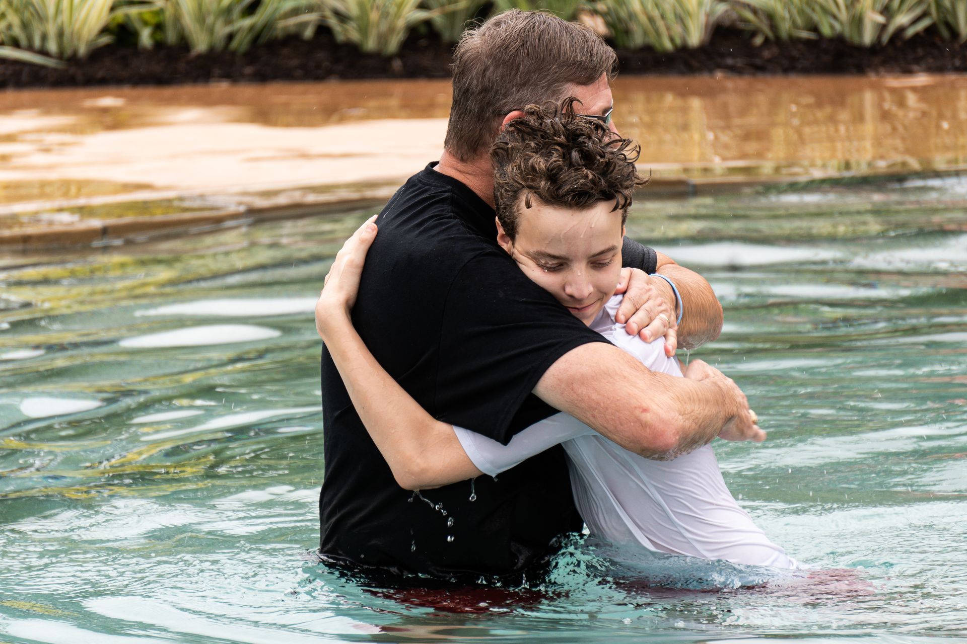 A man is hugging a young boy after a baptism in a pool of water.