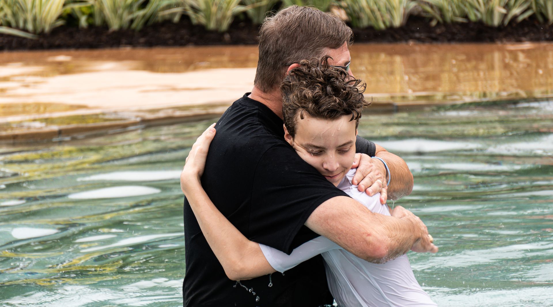 A man is hugging a young boy in the water.