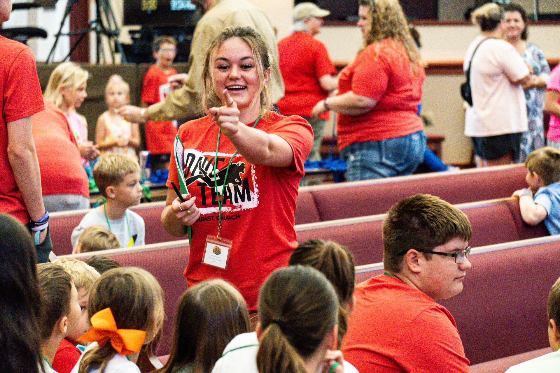 A woman in a red shirt is giving a thumbs up to a group of children in a church.