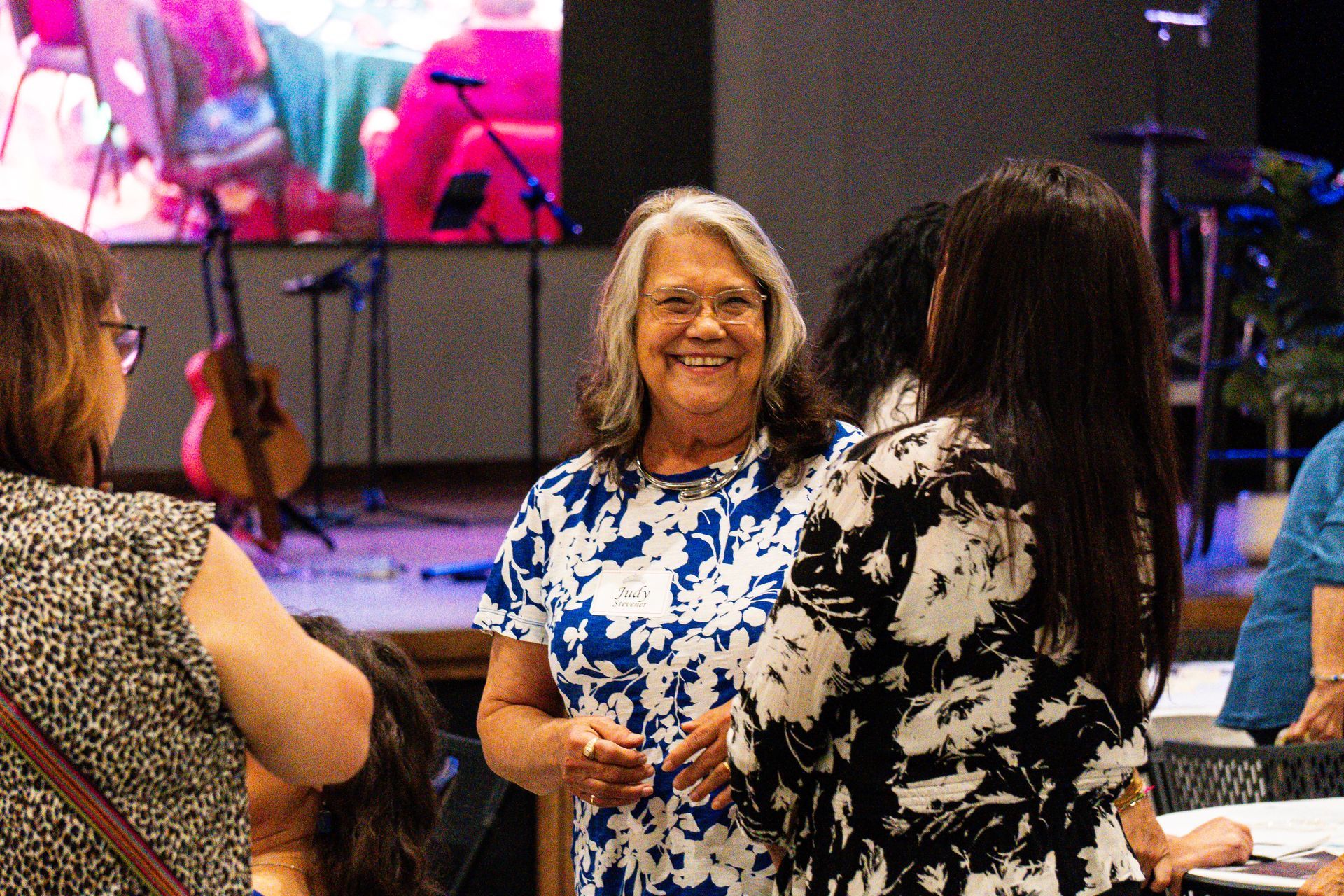 A group of women are standing in a room talking to each other.
