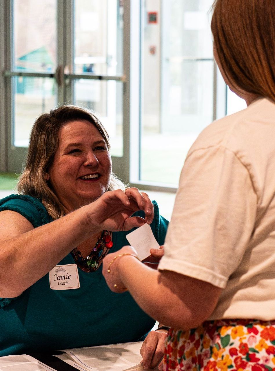 A woman is sitting at a table handing a paper to another woman.