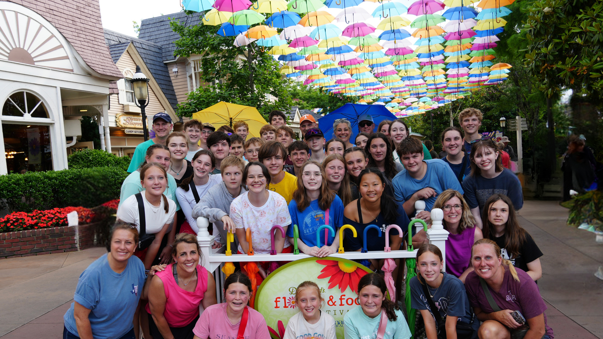 A group of people are posing for a picture in front of a wall of umbrellas.