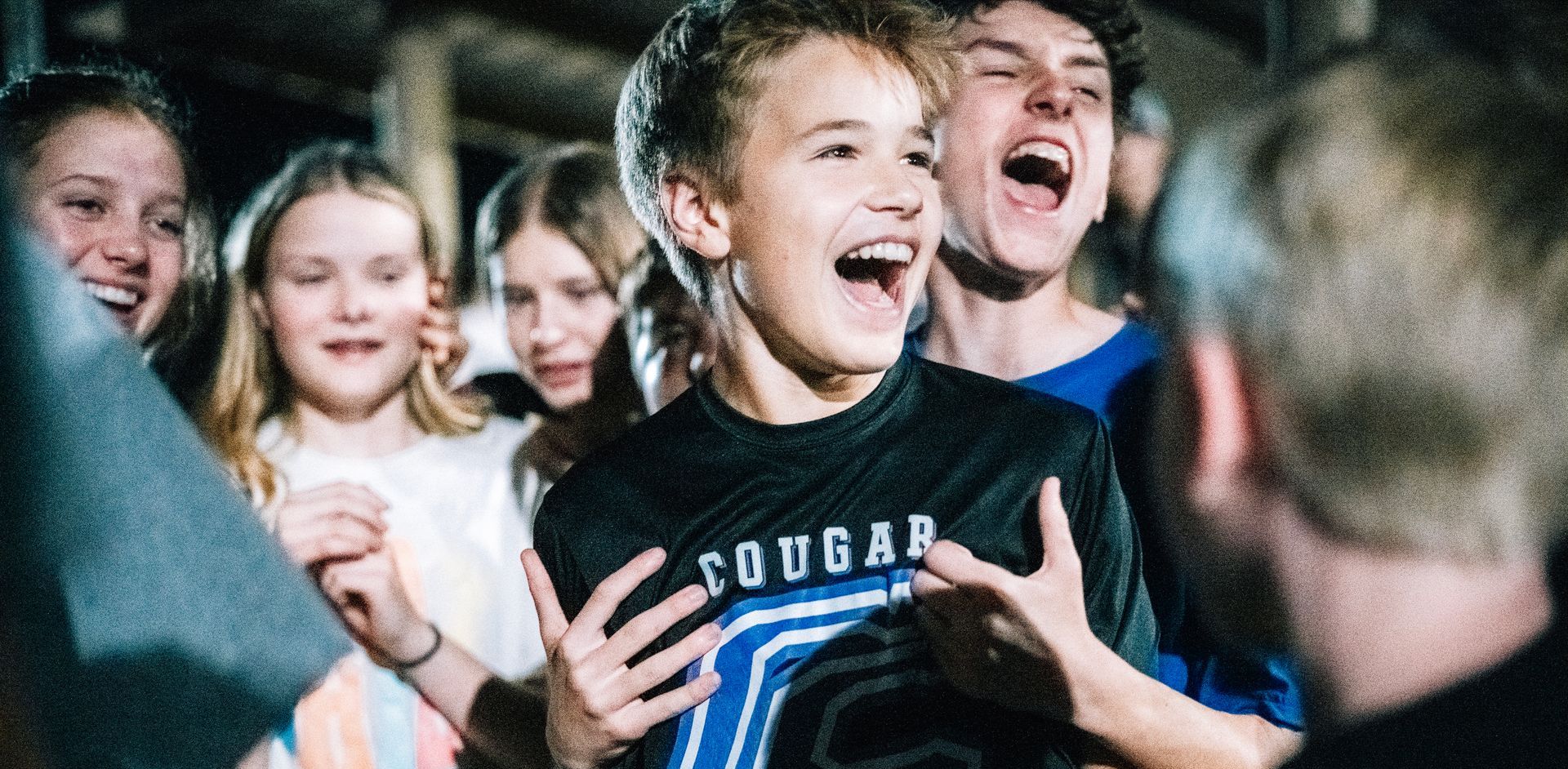 A group of young people are standing around a boy wearing a cougar shirt.