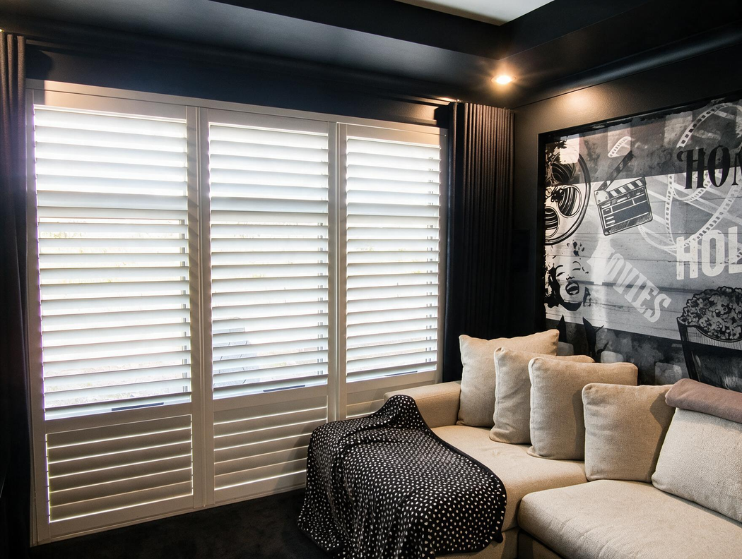 Modern living room with beige sectional, black throw, shuttered window, and monochrome wall art