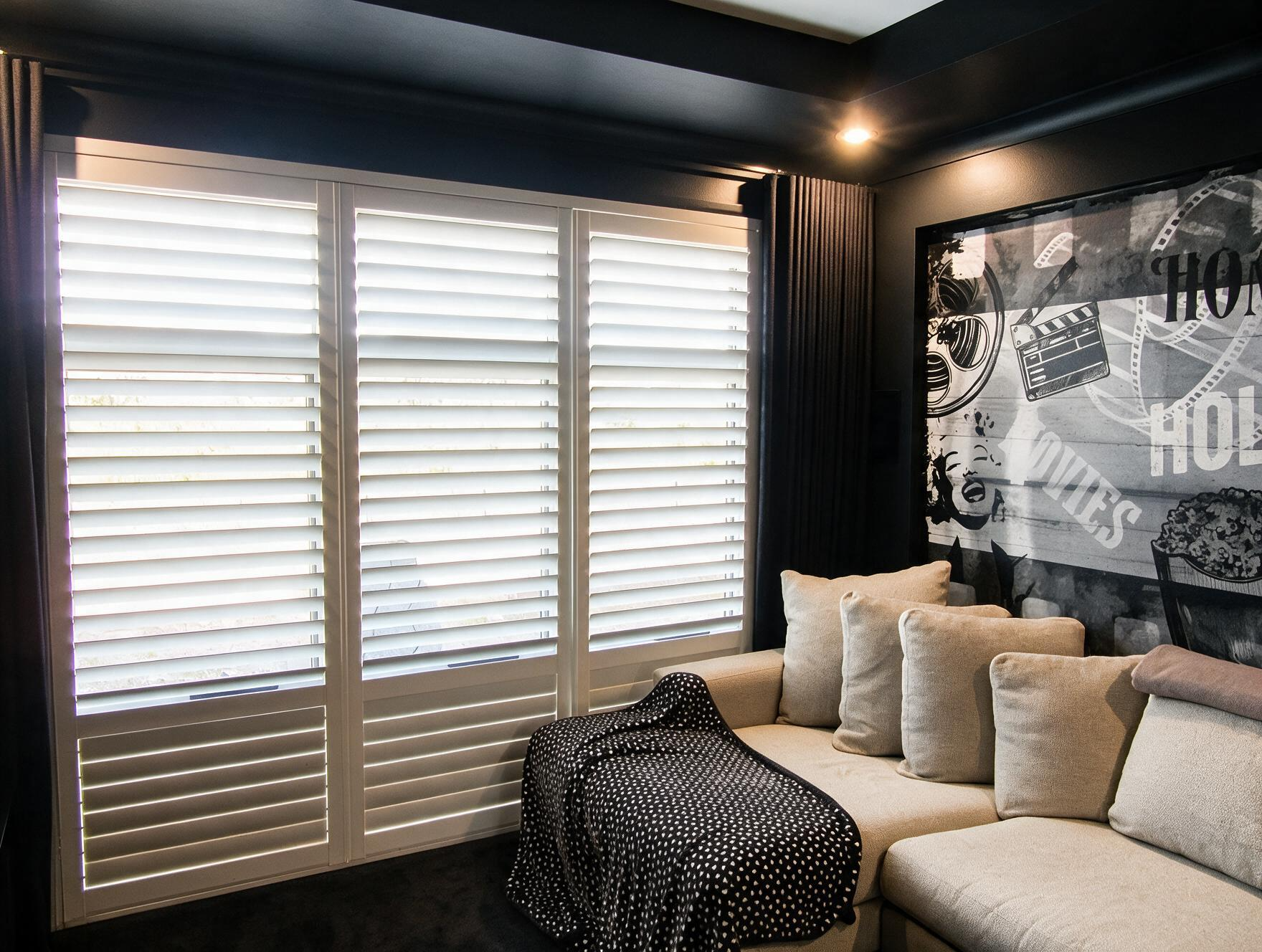 Modern living room with beige sectional, black throw, shuttered window, and monochrome wall art