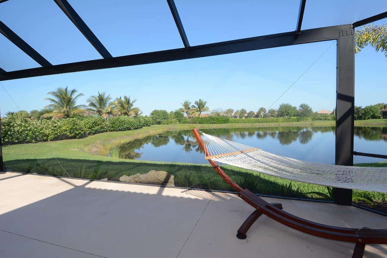Patio hammock overlooking a calm pond, green lawn, and palm trees under a blue sky