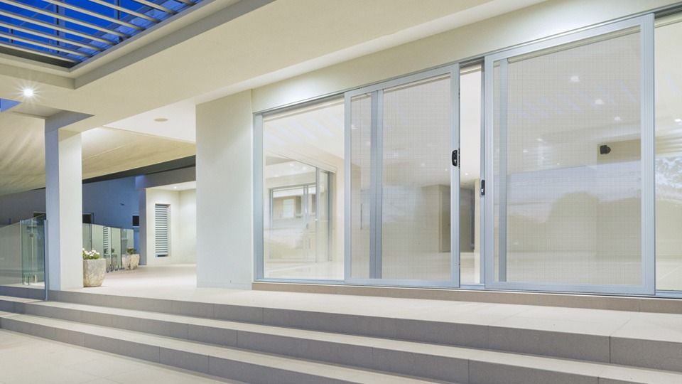 Modern building entrance with glass doors, white columns, and striped steps under a blue ceiling.