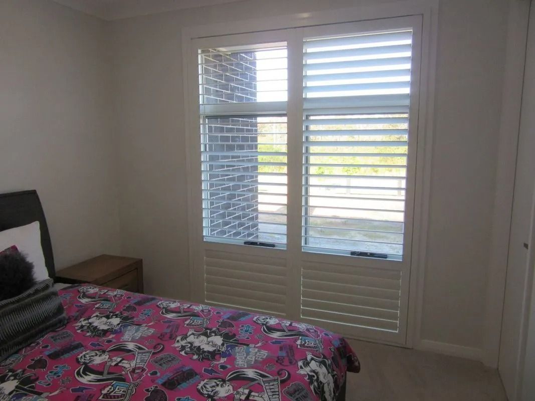 Bedroom with a bed, pink floral bedding, and a large window with white shutters.