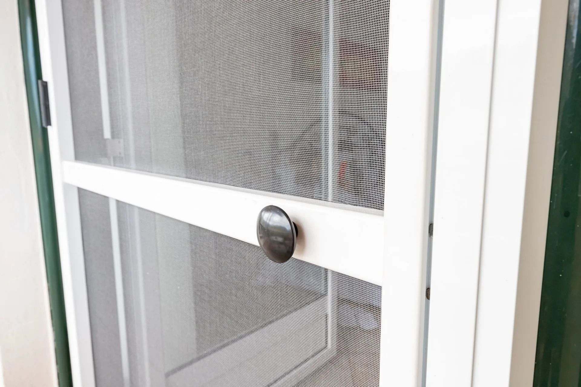 Close-up of a white screen door with a mesh panel and round silver knob