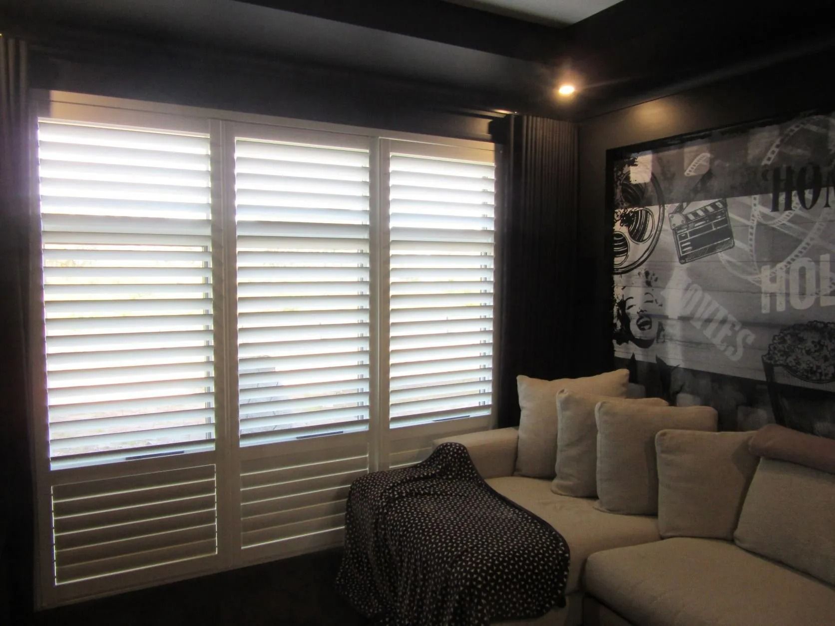 Modern bedroom with beige sofa, patterned ottoman, wall art, and bright window shutters