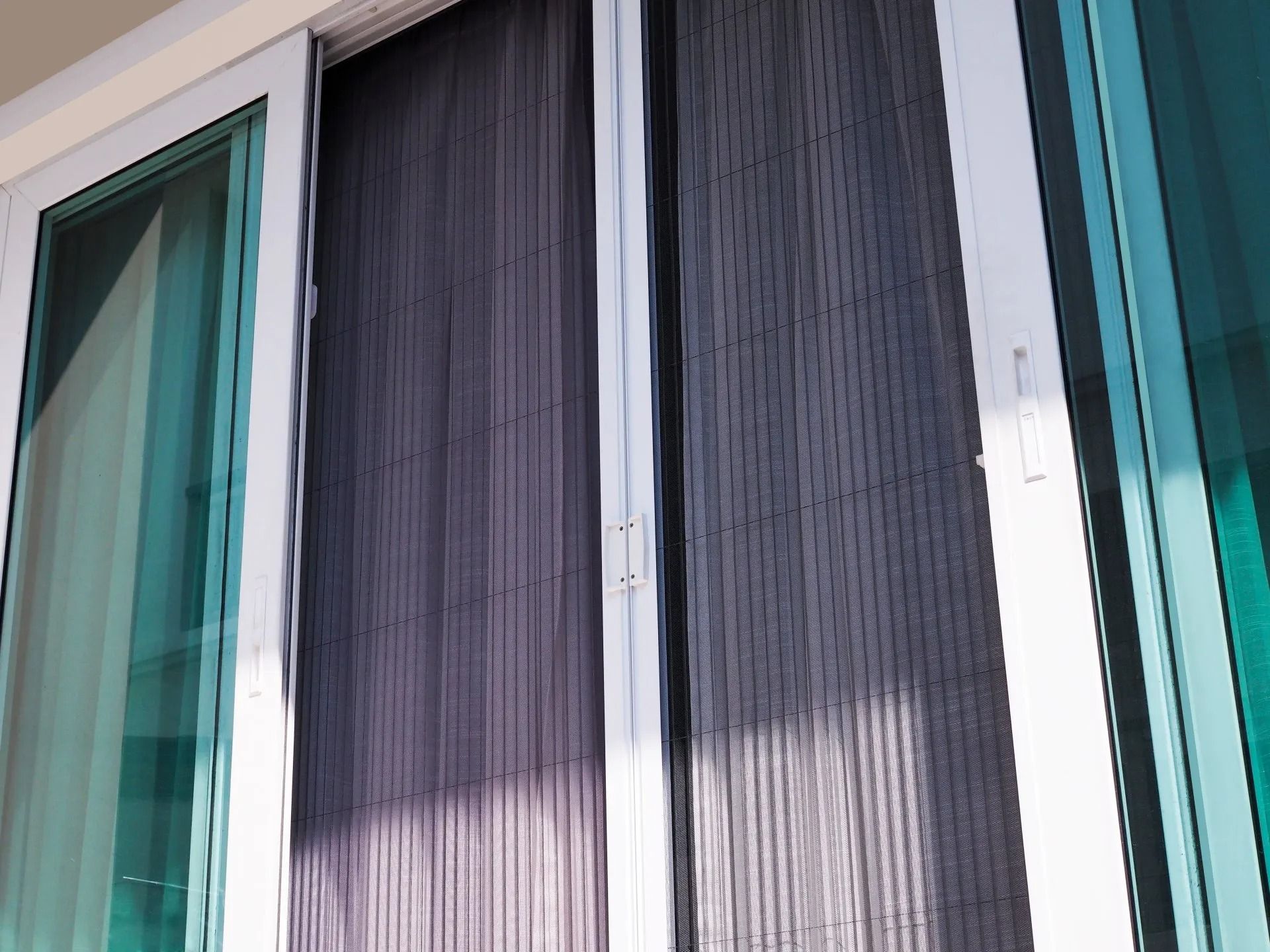 Sliding glass door with gray vertical blinds and turquoise trim, partially covered by sunlight and shadow