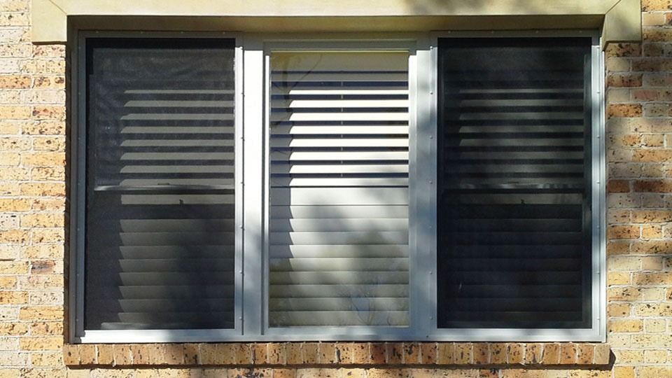 Three black window shutters flanking a central white louvered blind on a stone wall