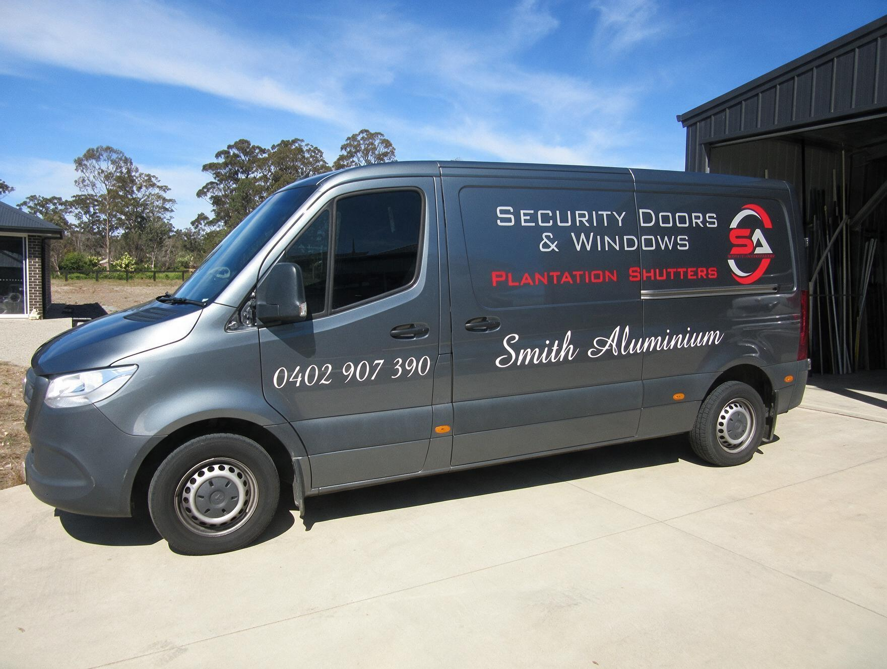Dark gray company van with security window branding parked outdoors in sunlight