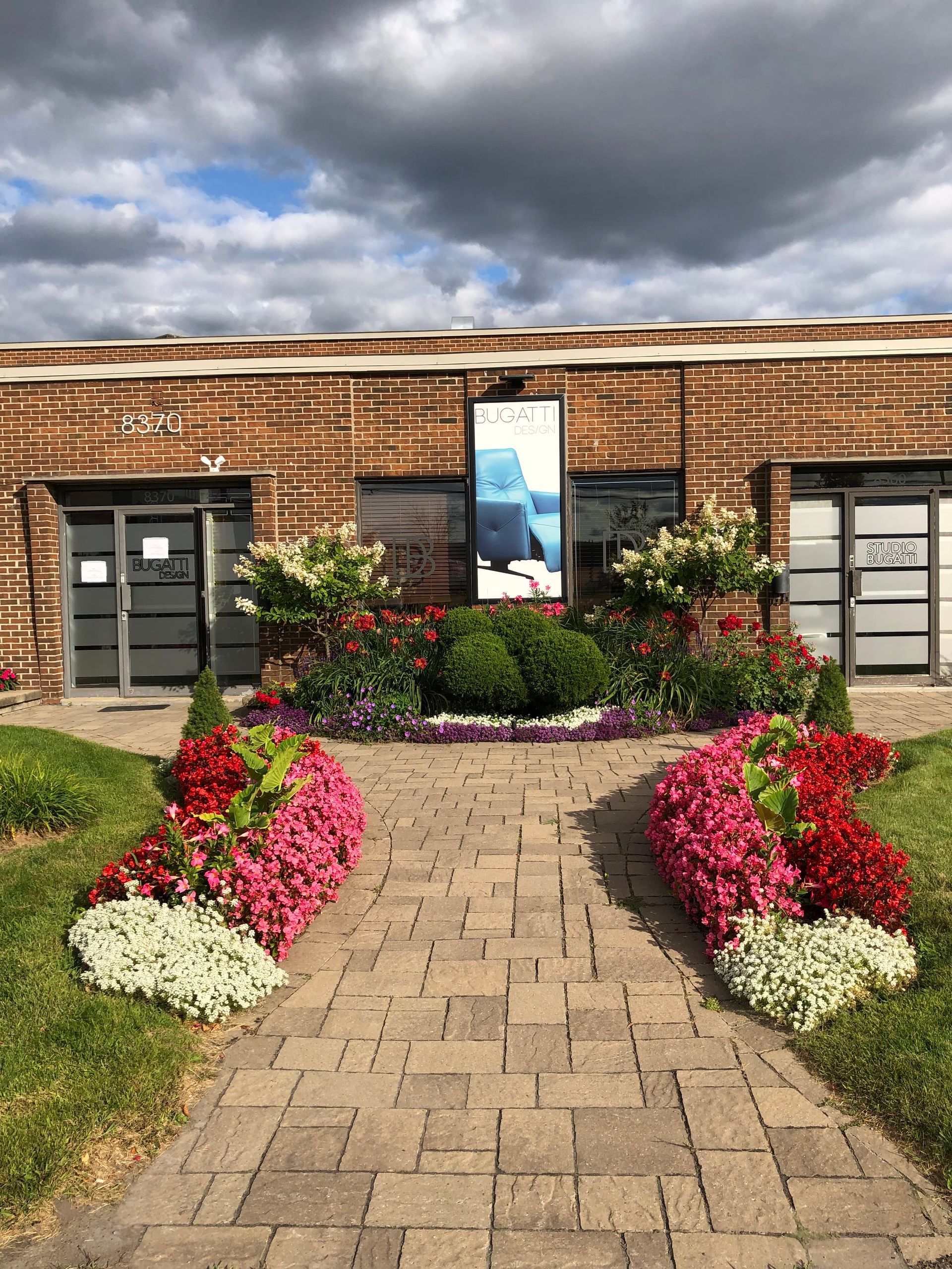 Une allée en briques menant à un bâtiment avec des fleurs devant.