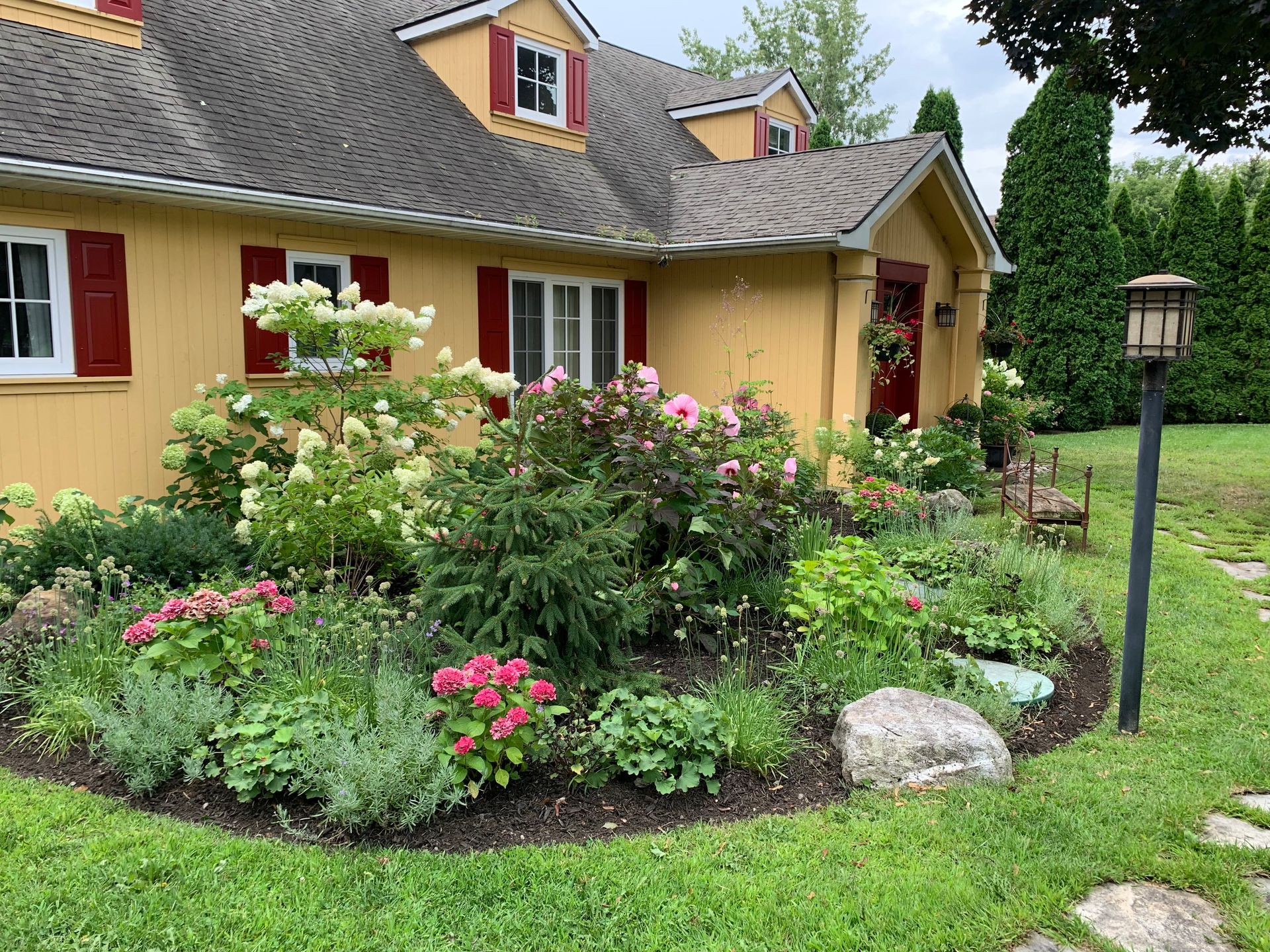 Une maison jaune avec des volets rouges et un jardin devant.